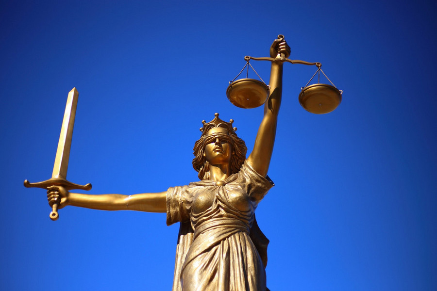 Statue der Justizia mit Schwert, Waage und verbundenen Augen vor blauem Himmel