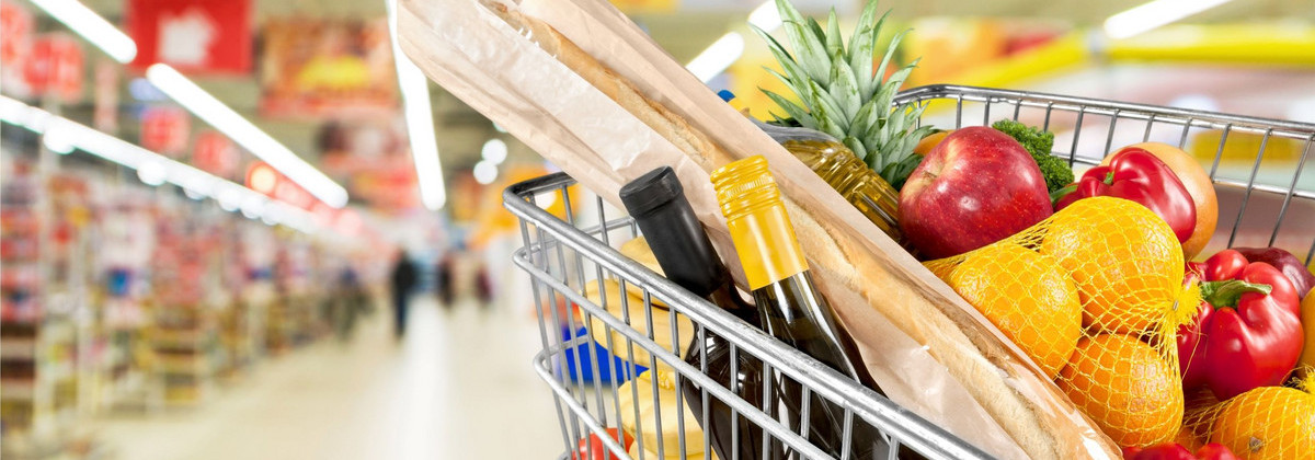 Das Bild zeigt einen vollen Einkaufwagen mit verschiedenen Lebensmitteln in einem Supermarkt. 