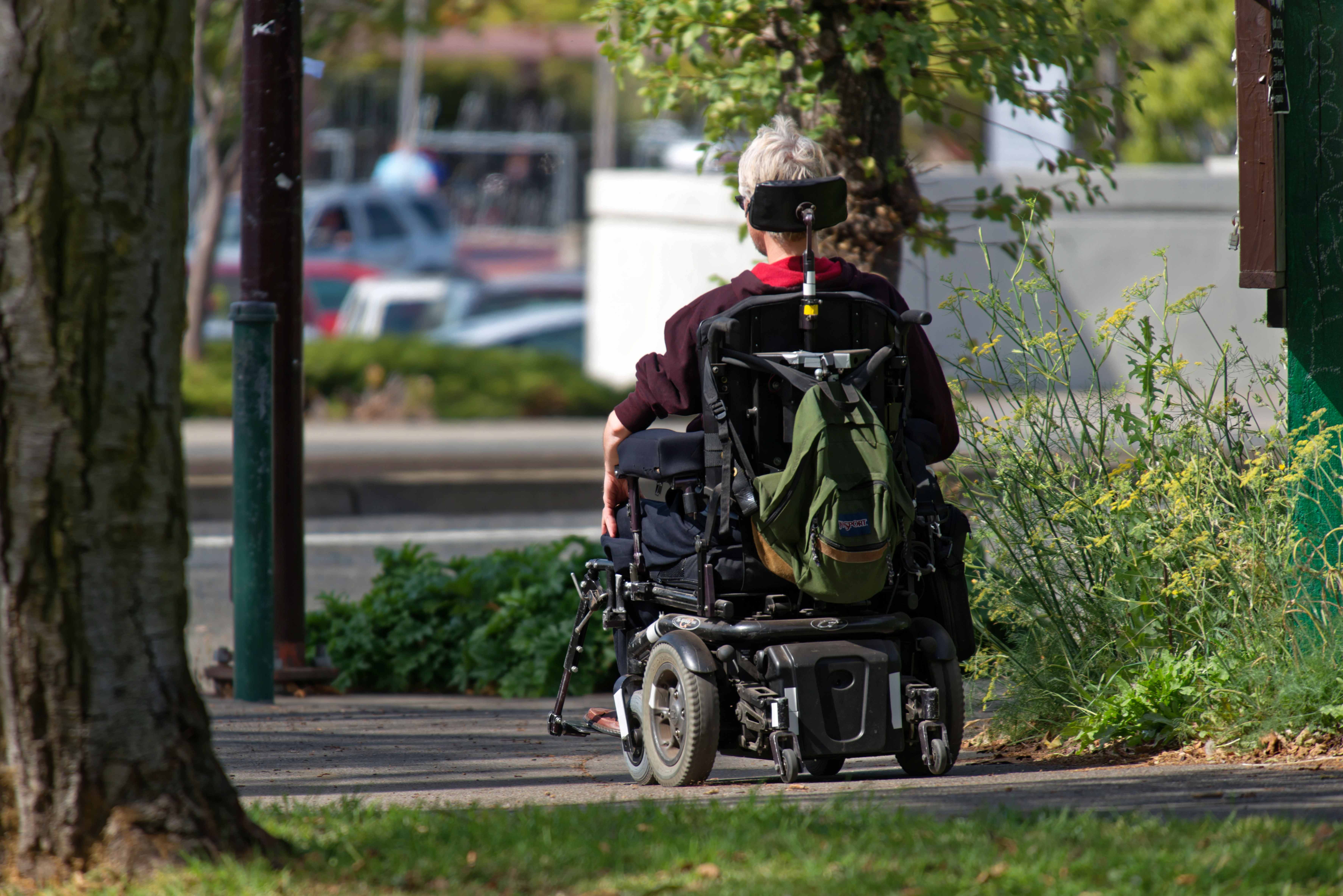 Mit dem Elektro-Rollstuhl unterwegs in der Stadt, schräg von hinten fotografiert