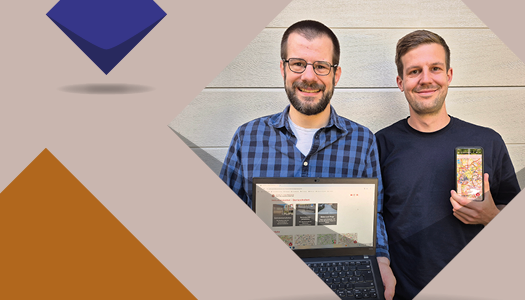 Zwei junge Männer halten einen Laptop und ein Handy mit Kartenmaterial ins Bild