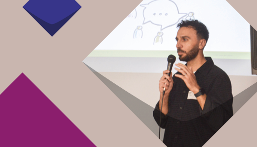 Ein junger man mit kurzen schwarzen Haaren hält einen Vortrag mit Microphone und im Hintergrund sieht man eine Präsentation