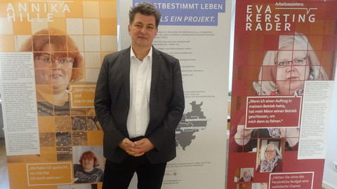 Tobias Fischer, Jurist beim KSL Düsseldorf, steht vor drei Elementen der Ausstellung zum Persönlichen Budget