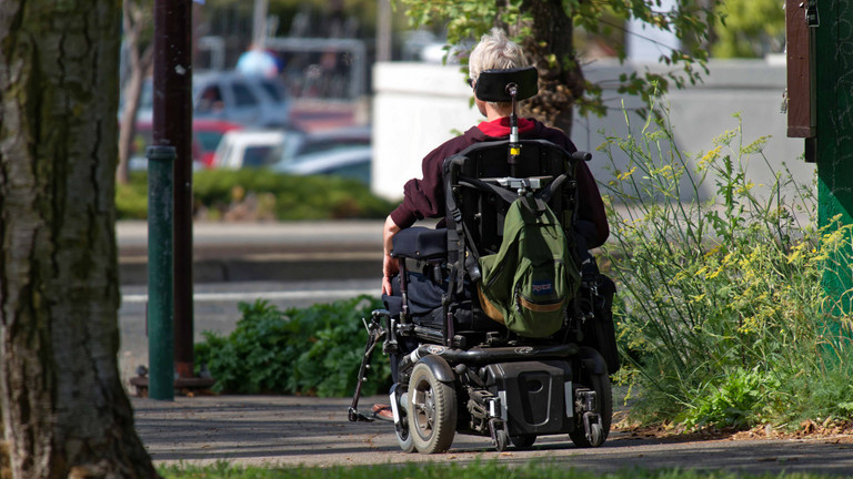 Mit dem Elektro-Rollstuhl unterwegs in der Stadt, schräg von hinten fotografiert
