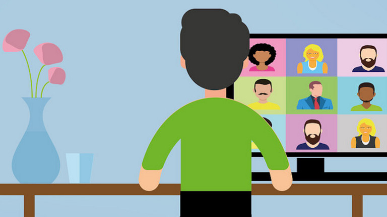 Das Bild zeigt eine Person, die am Tisch sitzt und eine Videokonferenz verfolgt. 